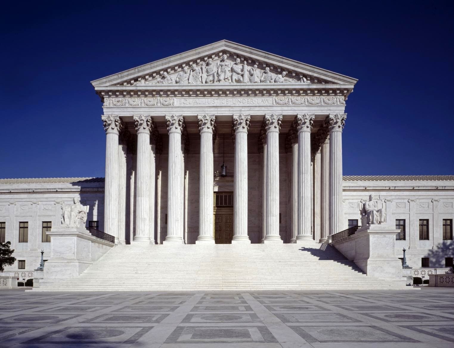 The U.S. Supreme Court building's broad front steps and columned main entrance, with EQUAL JUSTICE UNDER LAW carved above the columns, against a deep blue sky