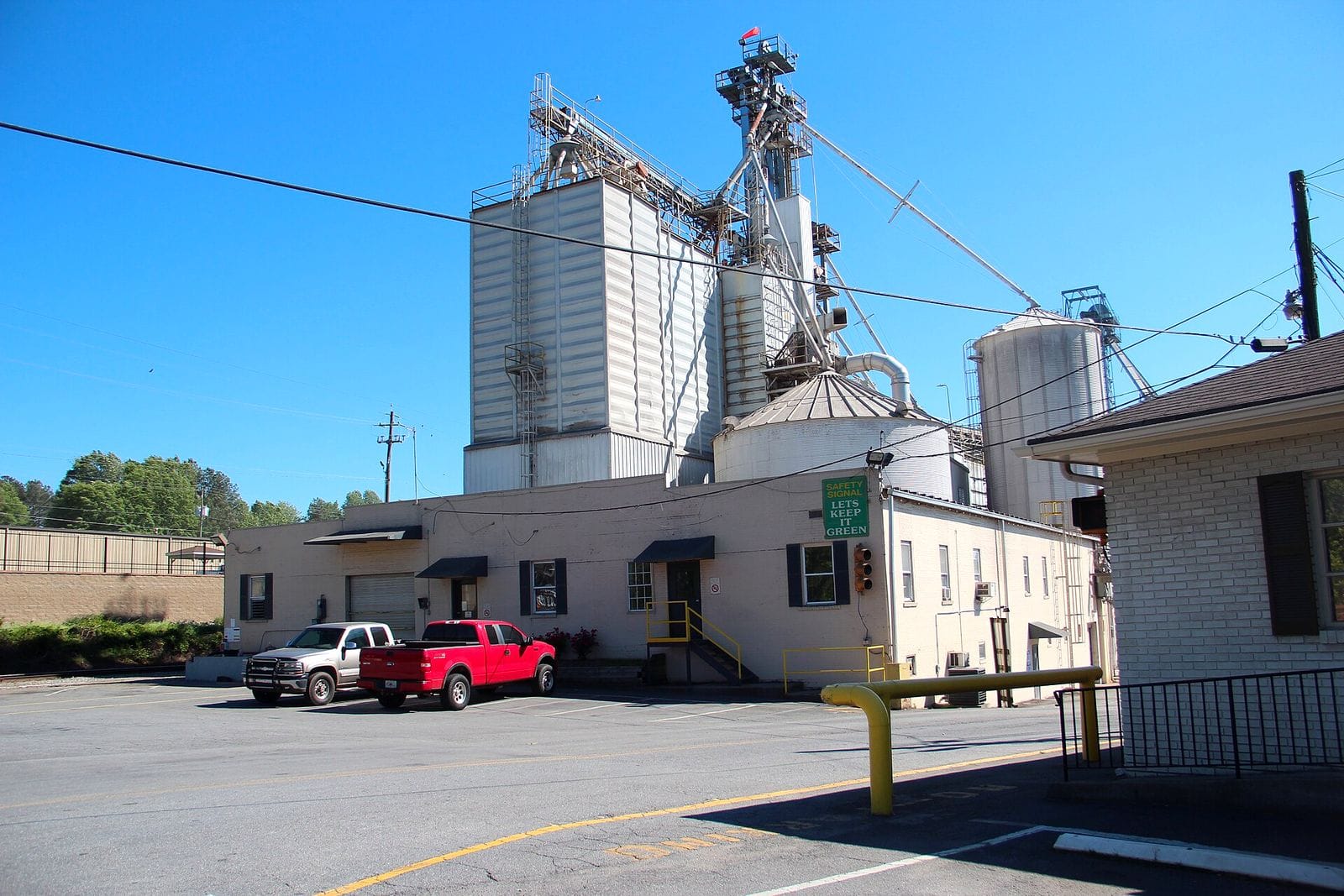 Grain silos and a low office building with pickup trucks parked outside at a Pilgrim's Pride facility in Univeter, Georgia