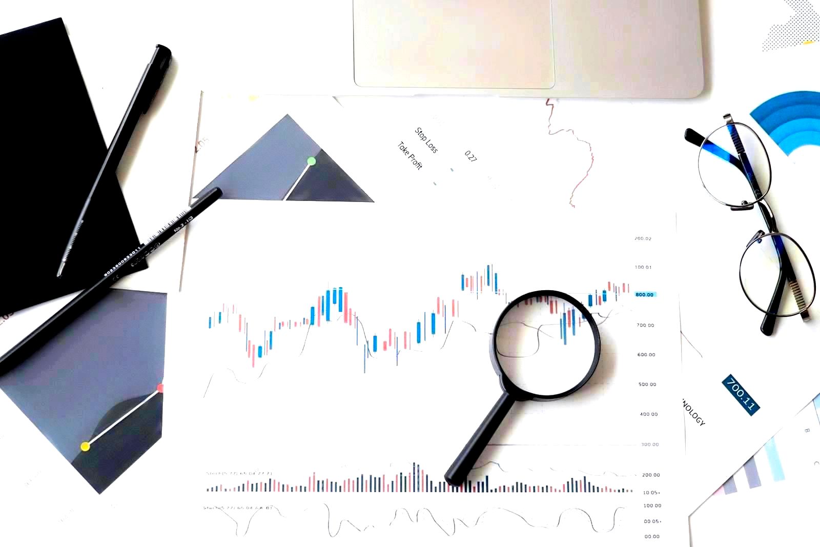 Stock market analysis documents with magnifying glass, pens, and glasses on a desk