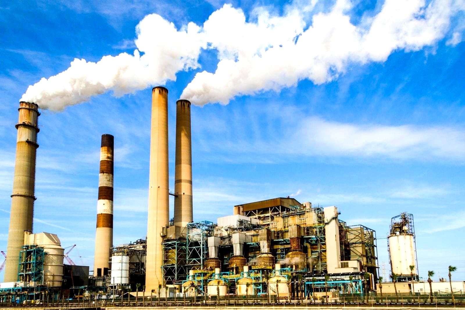 Industrial factory smokestacks emitting white steam against a cloudy sky