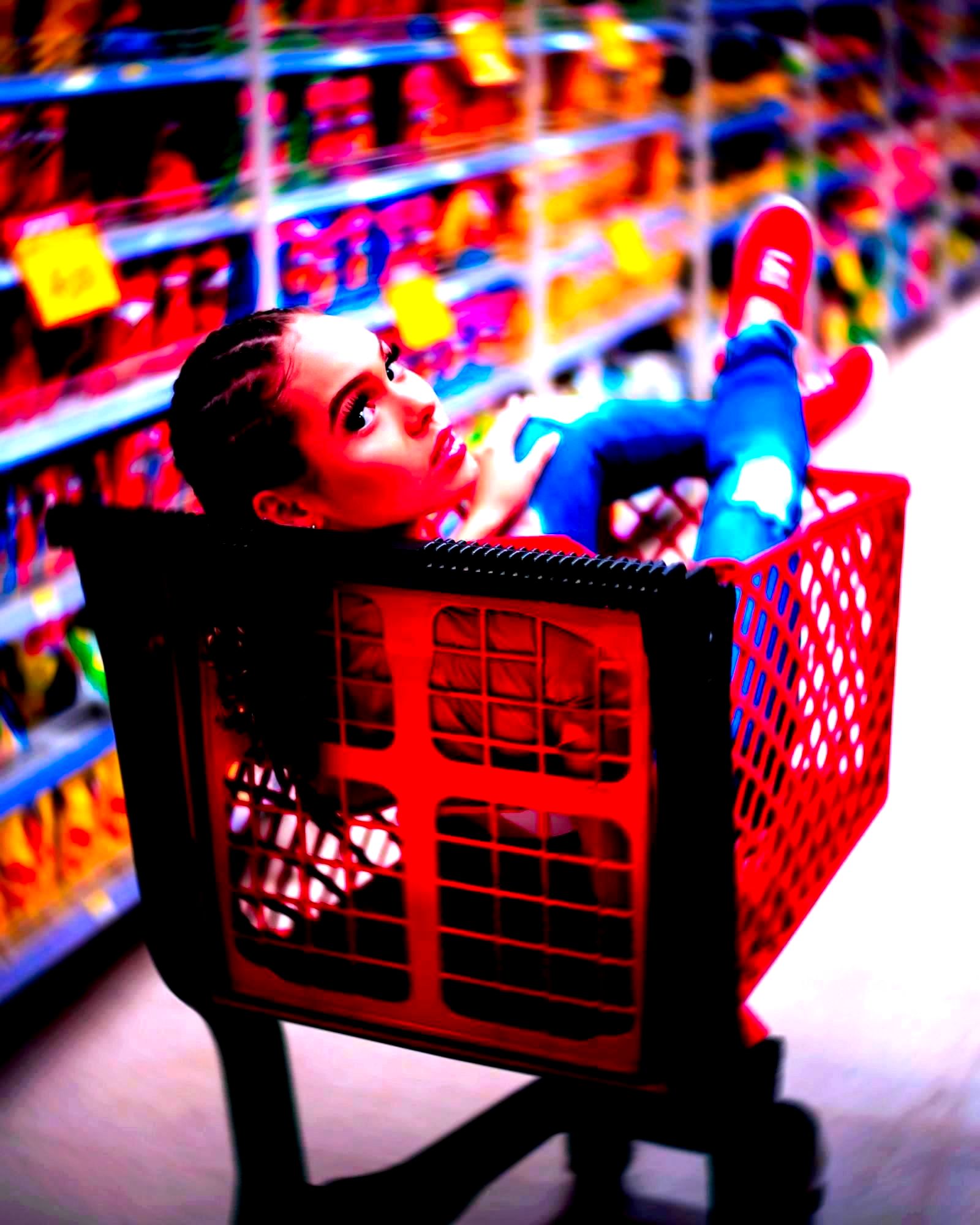 Woman standing in a red shopping cart in a retail store aisle