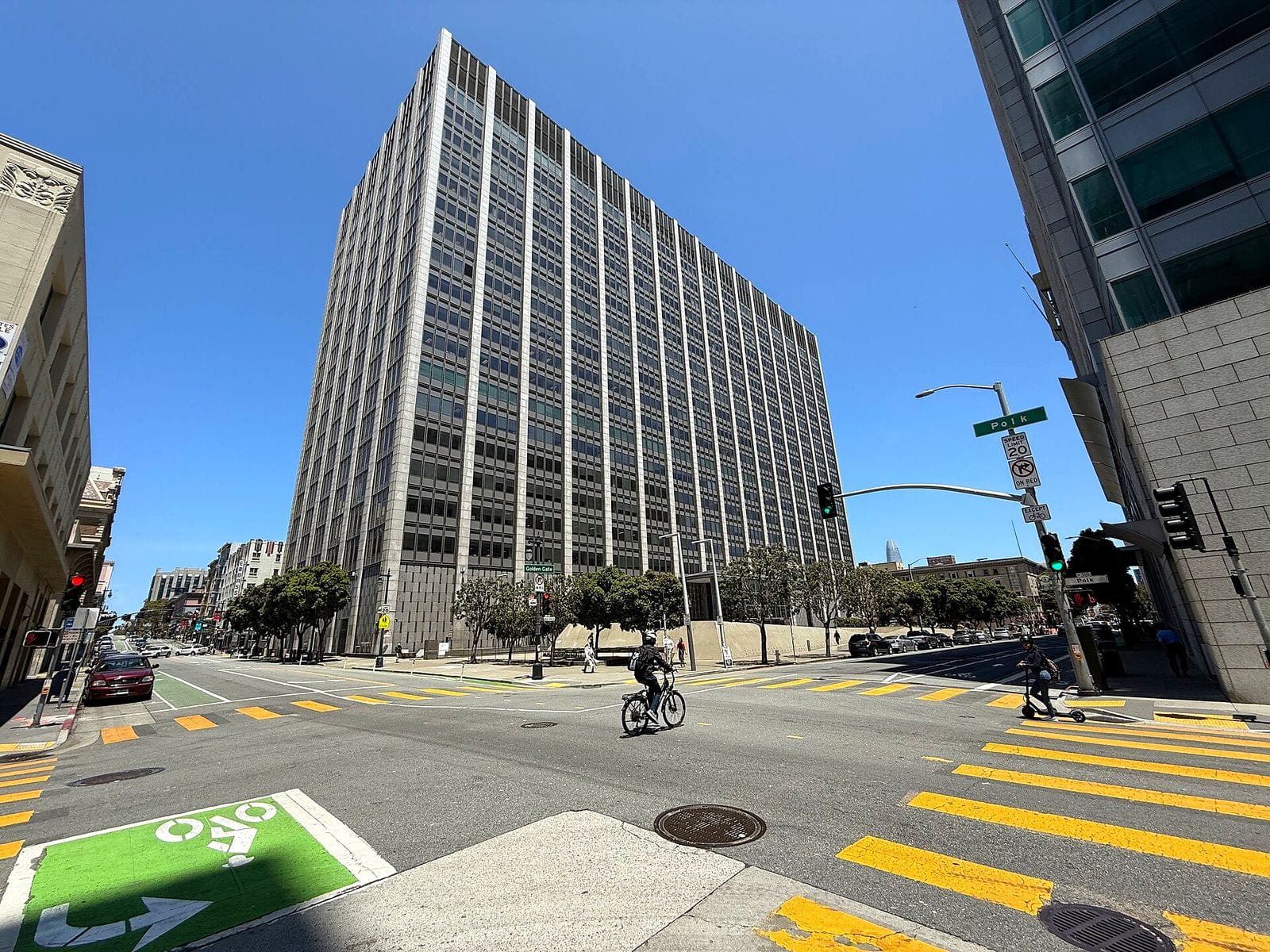 Phillip Burton Federal Building, a tall gridded office tower, seen across a San Francisco intersection with a cyclist in the crosswalk
